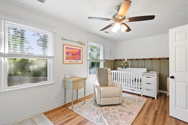 bedroom featuring wood finished floors, a crib, and ceiling fan