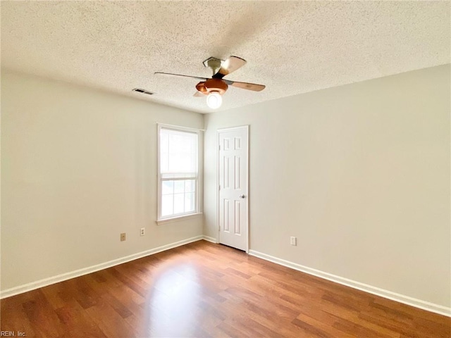 spare room featuring a ceiling fan, wood finished floors, baseboards, and a textured ceiling
