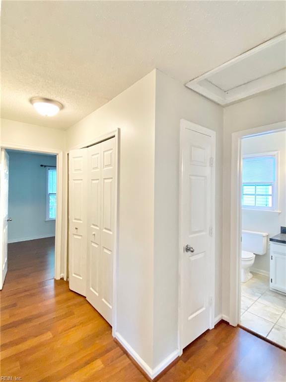 corridor with light wood finished floors, a textured ceiling, and baseboards