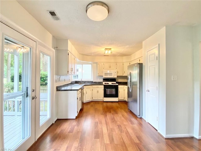 kitchen featuring range with gas cooktop, stainless steel refrigerator with ice dispenser, white microwave, dark countertops, and a sink