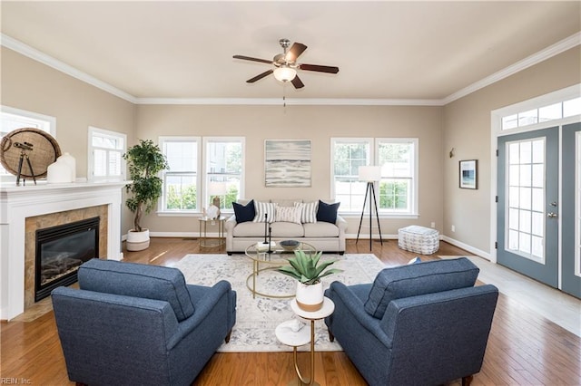 living area featuring a ceiling fan, ornamental molding, a fireplace, wood finished floors, and baseboards