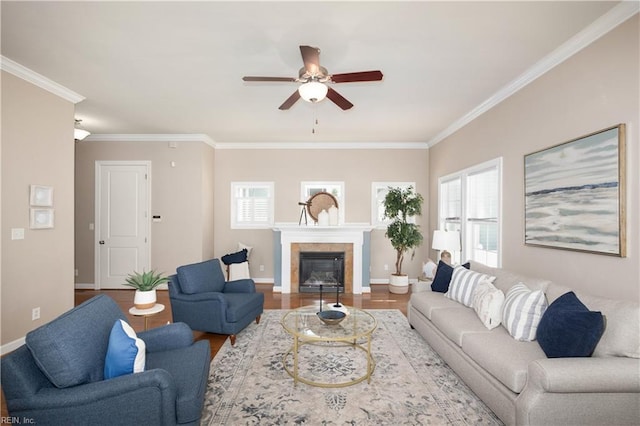 living area with ornamental molding, a ceiling fan, baseboards, wood finished floors, and a tile fireplace