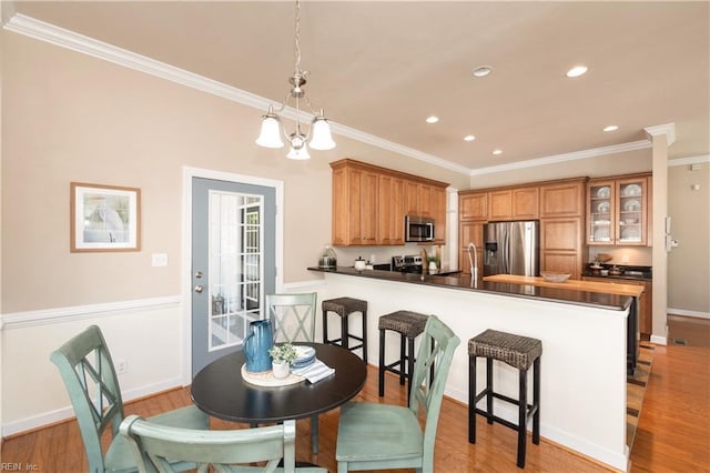 kitchen with stainless steel appliances, a breakfast bar area, ornamental molding, light wood-style flooring, and a peninsula