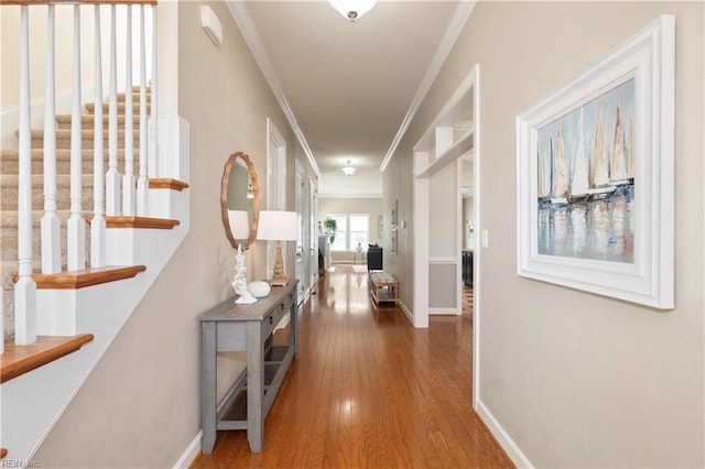 hall with ornamental molding, wood finished floors, baseboards, and stairway