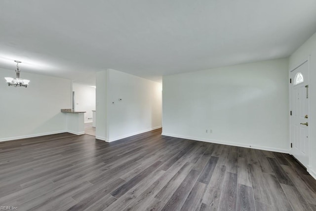 unfurnished living room with a chandelier, dark wood finished floors, and baseboards
