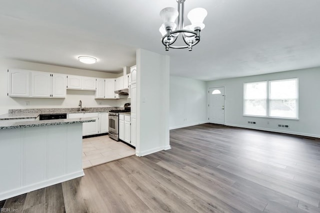 kitchen featuring stainless steel gas range, light stone countertops, a chandelier, a sink, and white cabinetry