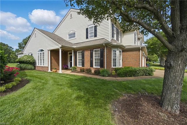 view of front facade with brick siding, a front yard, and a shingled roof