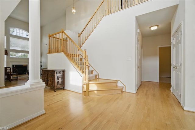 staircase featuring wood finished floors, a high ceiling, baseboards, and decorative columns