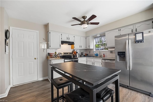 kitchen featuring stainless steel appliances, under cabinet range hood, tasteful backsplash, a ceiling fan, and dark wood finished floors