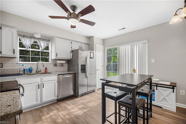 kitchen with appliances with stainless steel finishes, backsplash, light wood-style floors, white cabinetry, and ceiling fan