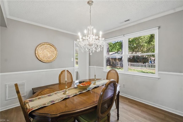 dining room with wood finished floors, a chandelier, a textured ceiling, baseboards, and crown molding