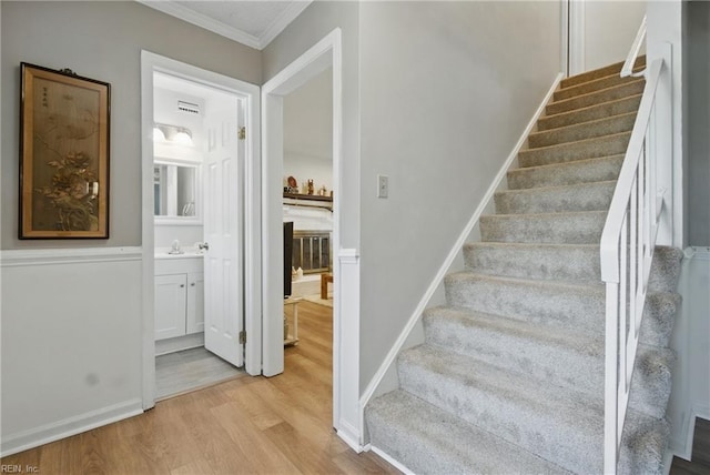 staircase with wood finished floors, ornamental molding, and baseboards