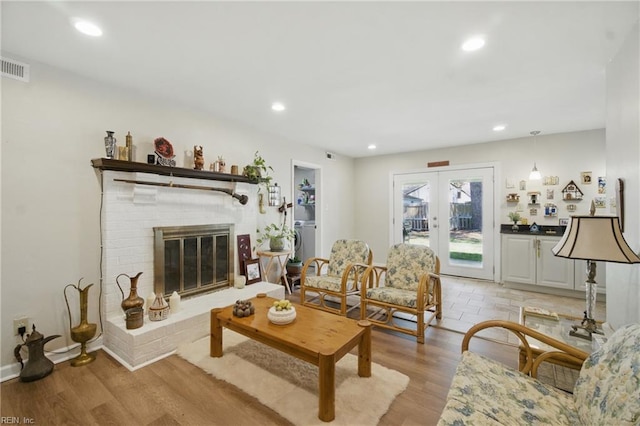 living area featuring light wood-type flooring, french doors, a fireplace, and recessed lighting