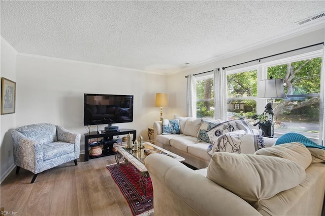 living area with wood finished floors, a textured ceiling, ornamental molding, and baseboards