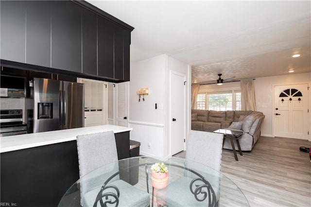 dining room featuring a ceiling fan, light wood finished floors, and a wainscoted wall