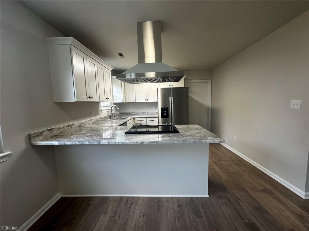 kitchen with stainless steel fridge with ice dispenser, island range hood, a sink, black electric cooktop, and baseboards