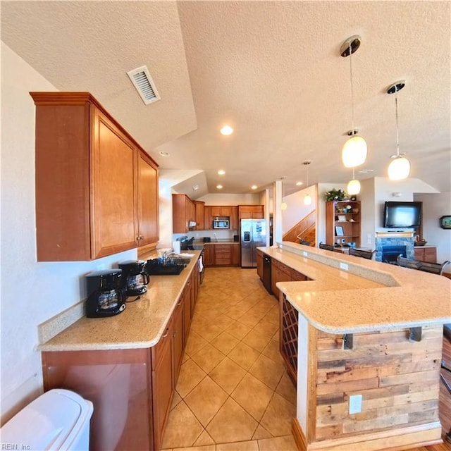 2390 Sandfiddler Rd, Corolla, NC 27927 - kitchen with stainless steel appliances, a textured ceiling, brown cabinetry, light stone counters, and decorative light fixtures