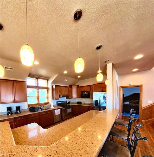 2390 Sandfiddler Rd, Corolla, NC 27927 - kitchen with appliances with stainless steel finishes, a textured ceiling, light stone countertops, brown cabinetry, and pendant lighting
