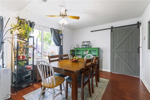 dining room featuring a ceiling fan, a barn door, wood finished floors, and baseboards
