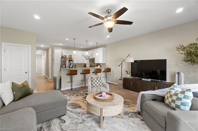 living room with a ceiling fan, recessed lighting, light wood-type flooring, and baseboards