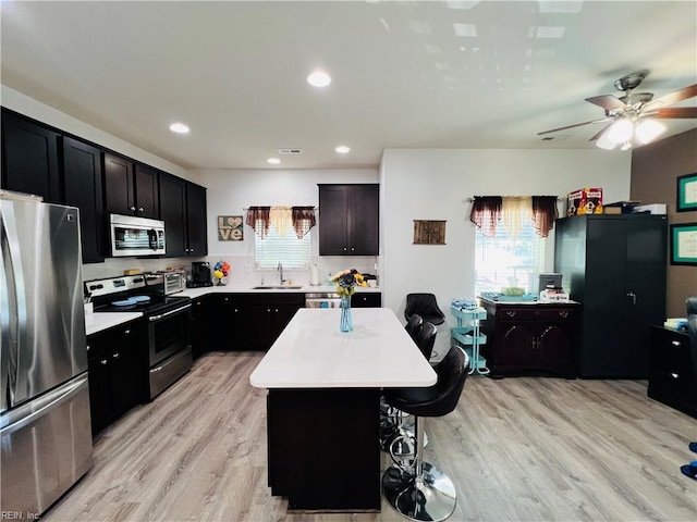 kitchen with stainless steel appliances, a kitchen island, a kitchen breakfast bar, light countertops, and light wood finished floors