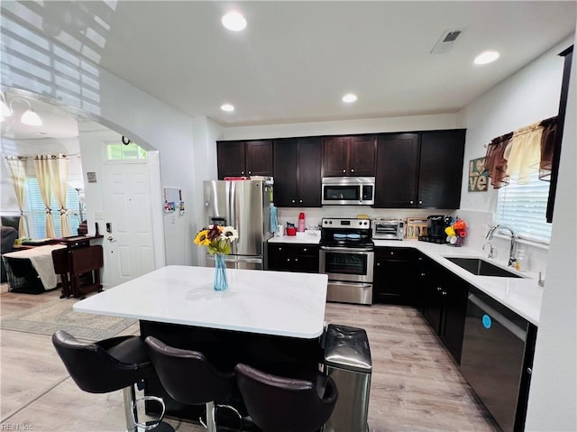 kitchen featuring stainless steel appliances, a sink, light countertops, a kitchen island, and recessed lighting