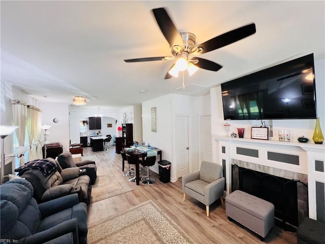 living room featuring light wood-type flooring, ceiling fan, and a fireplace