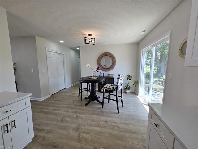 dining area featuring light wood finished floors, baseboards, a textured ceiling, and recessed lighting