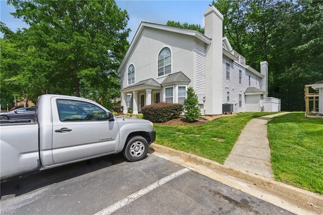 view of side of home featuring a lawn, uncovered parking, a chimney, and stucco siding