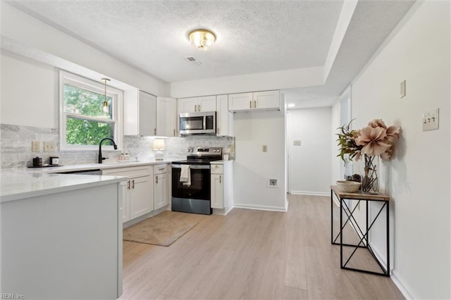 kitchen with appliances with stainless steel finishes, a sink, a textured ceiling, backsplash, and light wood-style floors