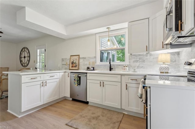 kitchen featuring stainless steel appliances, a sink, a peninsula, light wood finished floors, and white cabinets