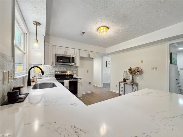 kitchen featuring stainless steel appliances, a sink, a textured ceiling, wood finished floors, and hanging light fixtures