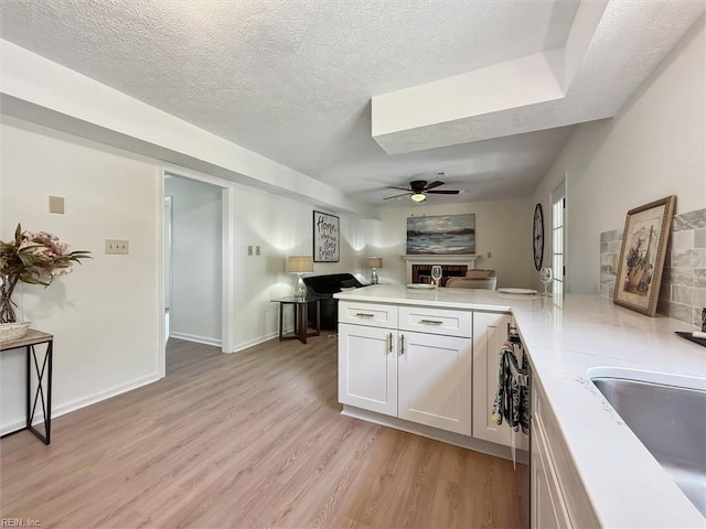 kitchen featuring light wood-style floors, ceiling fan, a peninsula, light countertops, and open floor plan