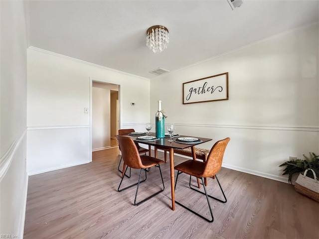 dining space featuring wood finished floors, crown molding, a chandelier, and baseboards