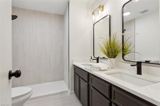 full bath featuring toilet, tiled shower, and double vanity