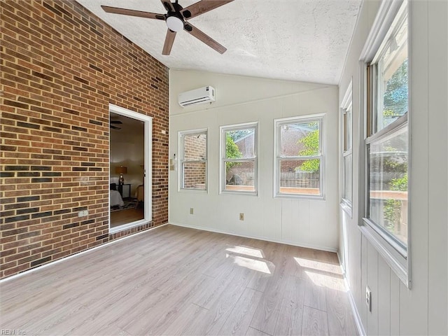 unfurnished sunroom with a wall unit AC, a textured ceiling, lofted ceiling, a ceiling fan, and wood finished floors