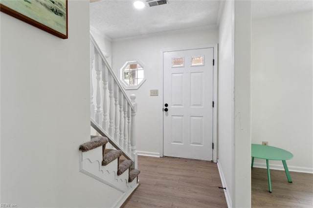 foyer with ornamental molding, stairway, wood finished floors, baseboards, and a textured ceiling