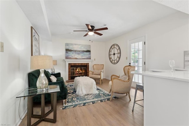 living area with ceiling fan, light wood-style flooring, and a brick fireplace