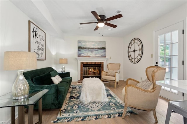 living room featuring ceiling fan, wood finished floors, a tiled fireplace, and baseboards