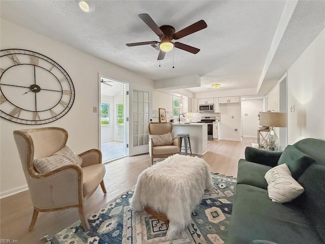 living area with a textured ceiling, a ceiling fan, baseboards, and light wood finished floors
