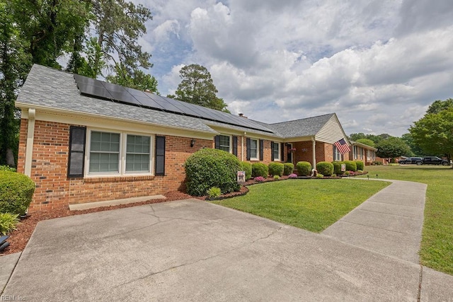 ranch-style house with brick siding, a front lawn, solar panels, and a shingled roof