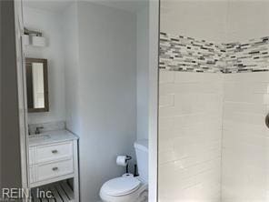 bathroom with a tile shower, vanity, and toilet
