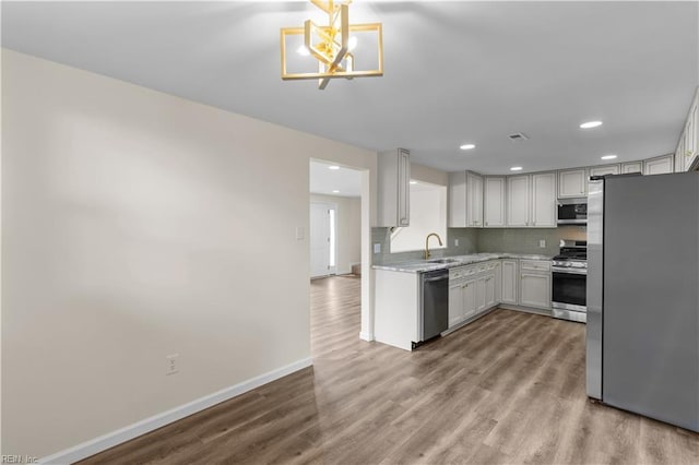 kitchen with appliances with stainless steel finishes, wood finished floors, baseboards, light countertops, and a chandelier