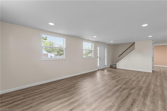 unfurnished living room featuring baseboards, light wood-style flooring, recessed lighting, and stairs