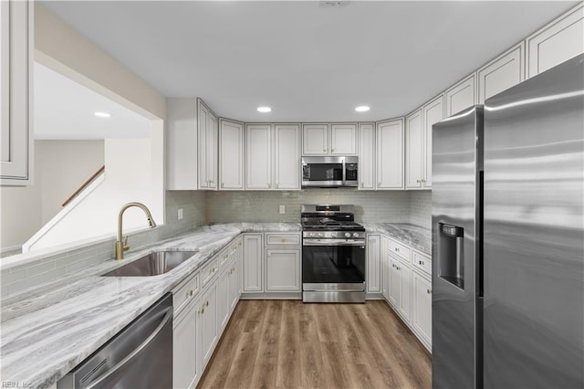 kitchen featuring appliances with stainless steel finishes, a sink, light wood-style flooring, light stone countertops, and recessed lighting