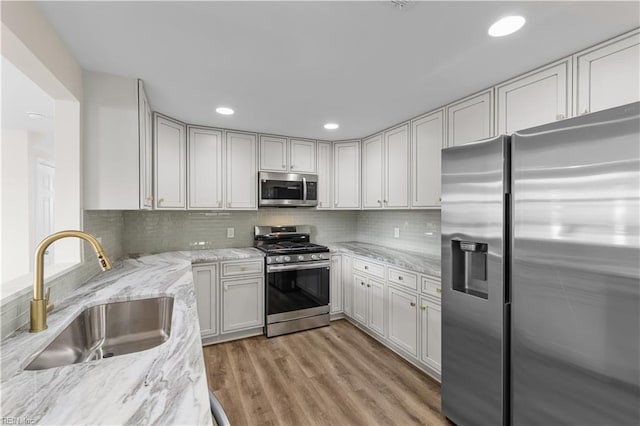 kitchen featuring appliances with stainless steel finishes, a sink, light stone counters, light wood finished floors, and decorative backsplash