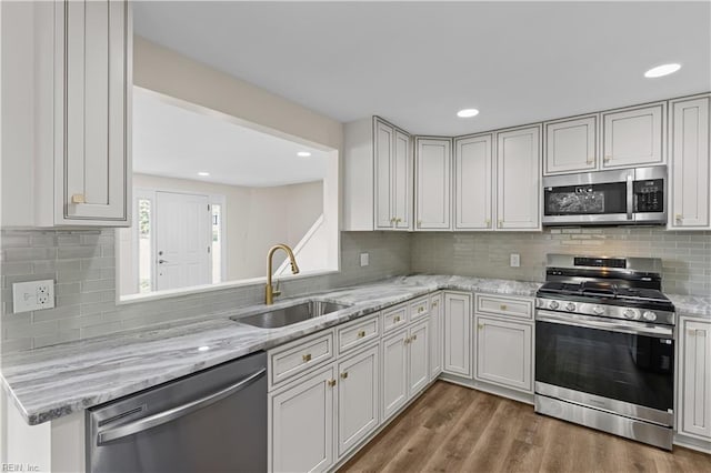 kitchen with appliances with stainless steel finishes, a sink, backsplash, wood finished floors, and recessed lighting
