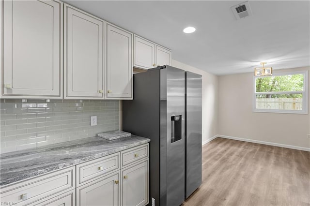 kitchen with stainless steel fridge with ice dispenser, baseboards, backsplash, light wood-type flooring, and light stone countertops