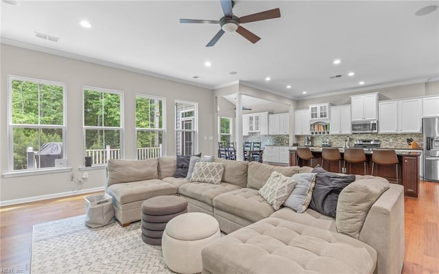 living area with a ceiling fan, crown molding, recessed lighting, light wood-style flooring, and baseboards
