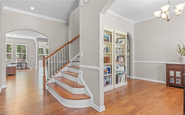 stairs with arched walkways, ornamental molding, wood finished floors, a chandelier, and recessed lighting